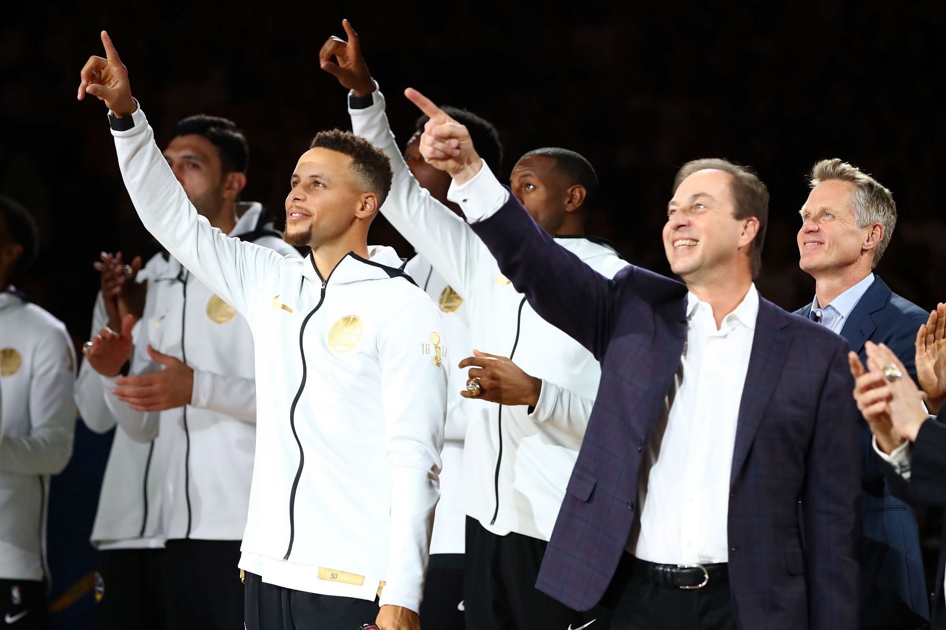 Steph Curry #30, owner Joe Lacob and the Golden State Warriors point to their 2017 NBA Championship banner prior to their NBA game against the Houston Rockets at ORACLE Arena on October 17, 2017 in Oakland, California.